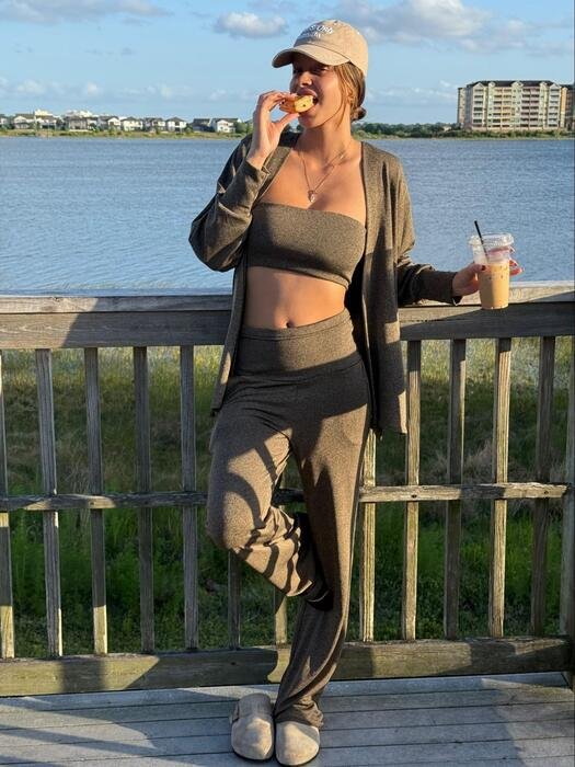 model com casaco c cropped malha freddo 106 caqui escuro comendo bolo e segurando bebida com mar ao fundo