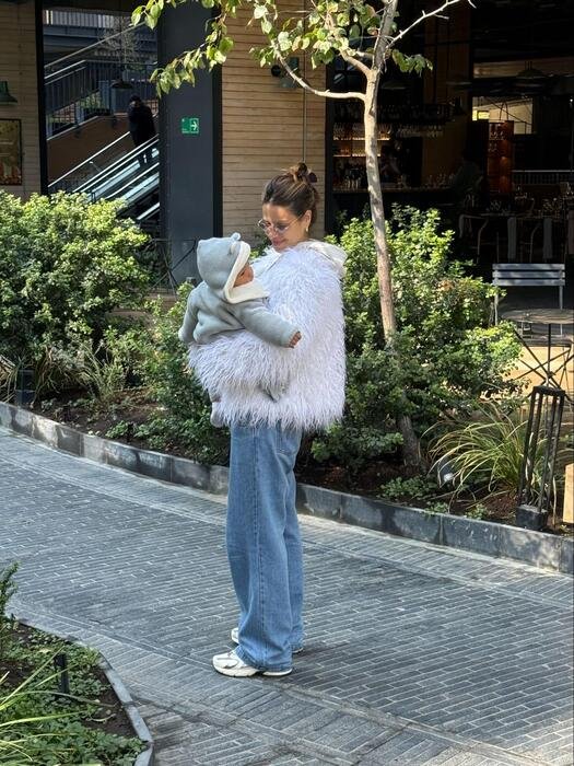 mae com calca jeans emma fiorezi casaco de plumas e oculos segurando bebe e olhando para ele